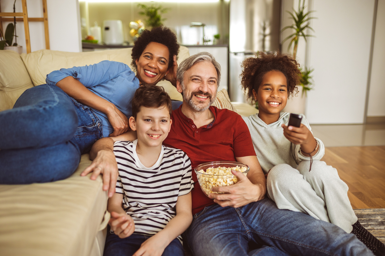 Young, interracial family watching TV together at home and having fun together.